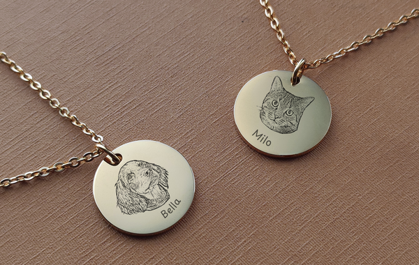Two gold necklaces with engraved pet portraits on round pendants against a brown background.